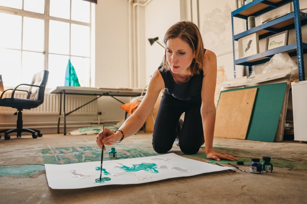 Photograph of artist Abi Spendlove painting with ink on her studio floor